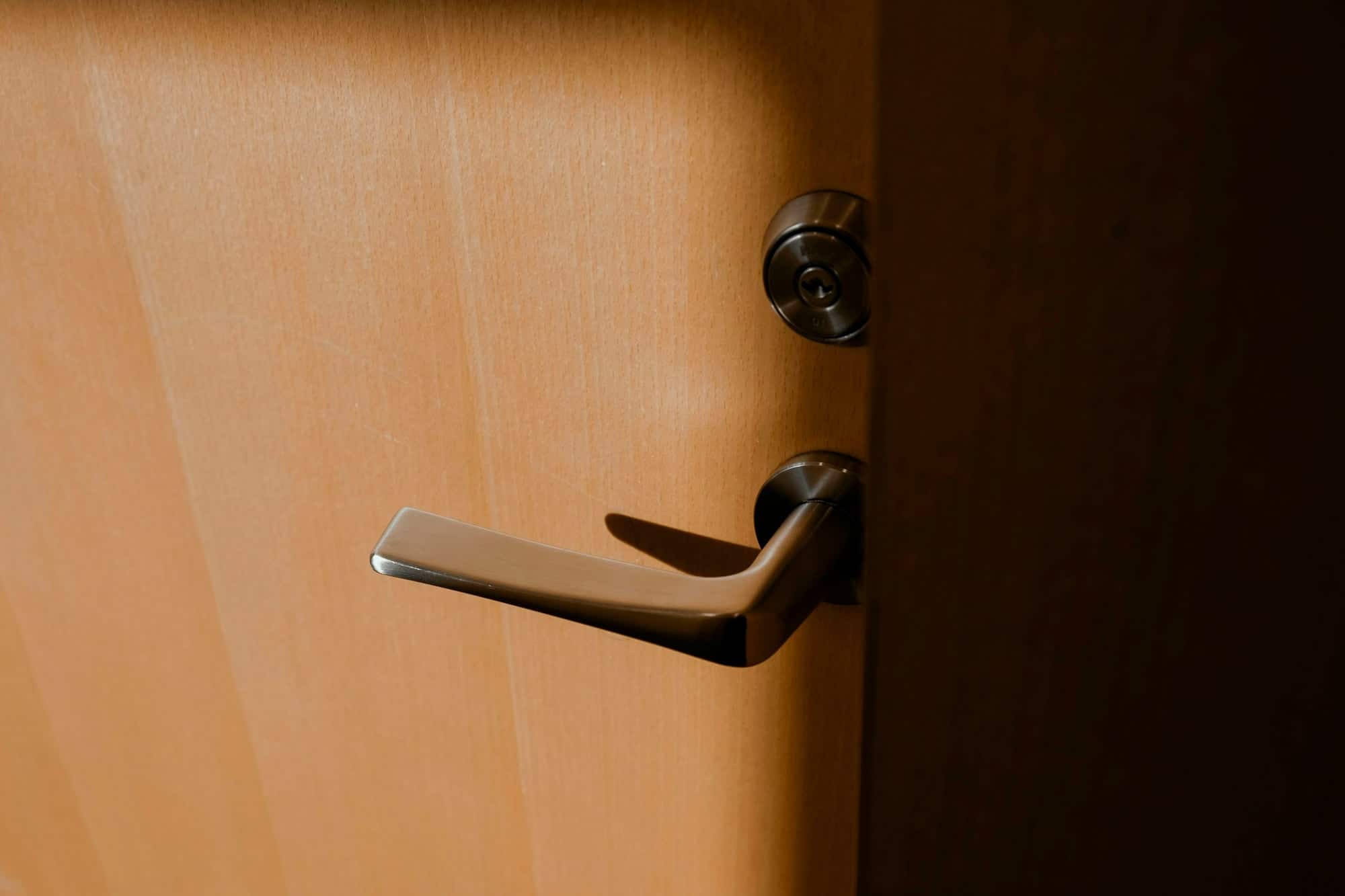 Gros plan d'une poignée de porte en métal et de son cylindre de serrure sur une porte en bois clair