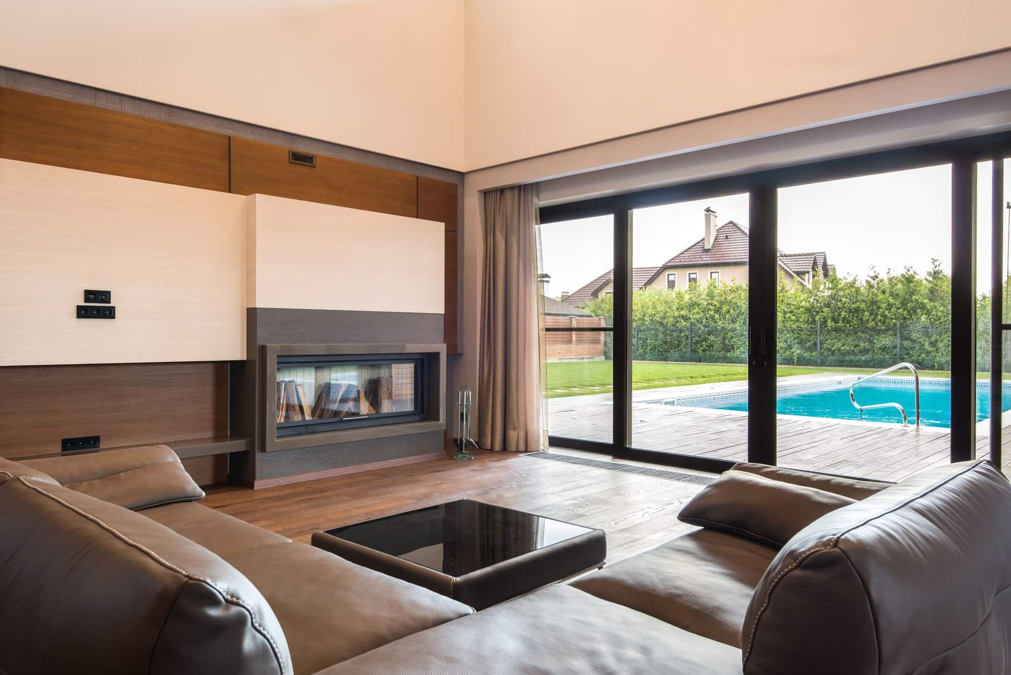 Salon lumineux ouvert par une grande baie coulissante à cadre aluminium noir sur une terrasse en bois et une piscine