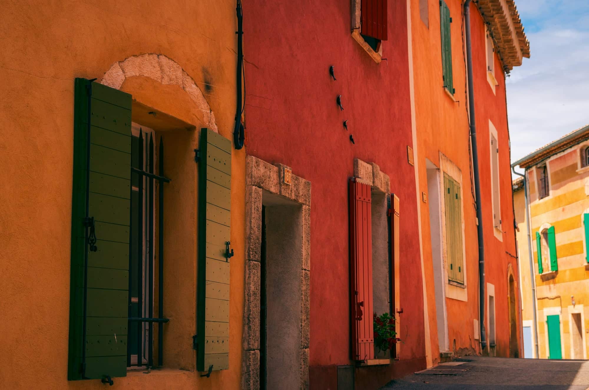 Ruelle de village provençal aux façades ocre et rouges, avec des volets battants en bois peints en vert